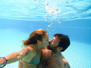Happy caucasian people couple have fun and enjoy the swimming activity at the pool - concept of holiday summer vacation in resort or hotel - underwater adult man and woman together with kiss and love