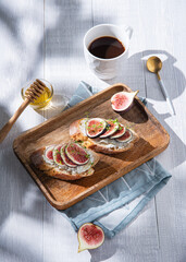 Breakfast with fig, cheese and honey sandwich on a wooden board and cup of coffee on white table