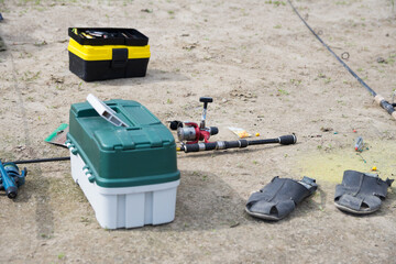Fishing on the sandy beach. fishing rods and a box with baubles and other fishing accessories on the river Bank. Focus on the red rod reel in the center