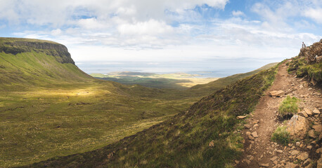 Fototapeta premium Panoramic view of large valley in Quiraing in summer. High angle view of the Trotternish landslip, Isle of Skye, Scotland. Sea and coastline in background