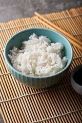 Rice in a porcelain bowl, with Japanese chopsticks, soy sauce, served on a gray stone table