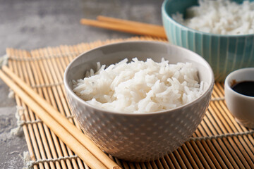 Rice in a porcelain bowl, with Japanese chopsticks, soy sauce, served on a gray stone table