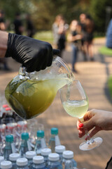 Catering. The waiter pours juice from a jug, lemonade in glass with hands. Summer, Sunny day. Banquet. Soft drink. Background image, copy space