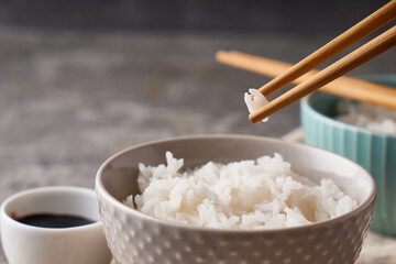 Fototapeta na wymiar Rice chopsticks, over a bowl of white rice, soy sauce on a dark gray background