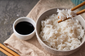 Rice chopsticks, over a bowl of white rice, soy sauce on a dark gray background