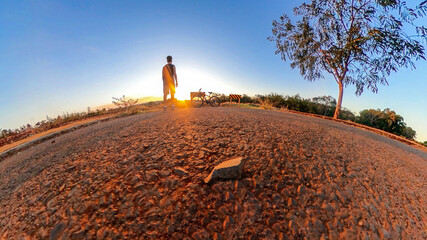 Man with bicycle on little planet with trees, soft blue sky and sunset. Mini planet of a park and...