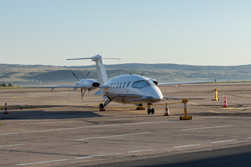 Side view of white business airplane with twin turboprop engines mounted in pusher configuration. Blue sky over the airport. Modern technology in fast transportation, business travel and tourism.  
