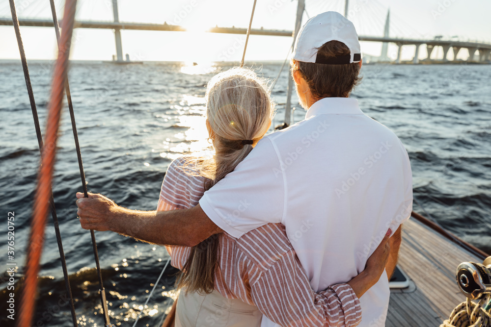 Wall mural Back view of two mature people hugging together. Senior couple standing on a yacht bow and looking into distance.