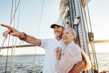 Mature man pointing into the distance and hugging his wife. Two smiling people enjoying a boat trip...