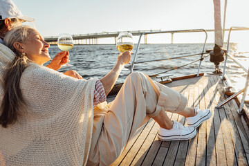 Mature man and woman wrapped in plaid on yacht deck and drinking wine. Senior couple holding...