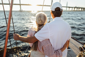 Back view of two mature people hugging together. Senior couple standing on a yacht bow and looking...