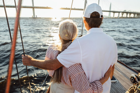 Back View Of Two Mature People Hugging Together. Senior Couple Standing On A Yacht Bow And Looking Into Distance.