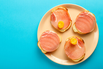 Sandwiches with ham and cherry on a plate on a blue background. Copy the place.