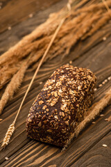 selective focus of fresh baked bread loaf with spikelets on wooden surface
