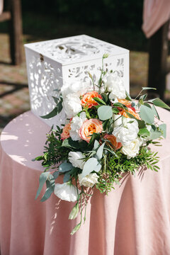 Front view of beautiful floral composition made of white, orange roses on table, wooden box for presents on wedding celebration. Tender furniture details for gifts. Concept of bridal interior elements