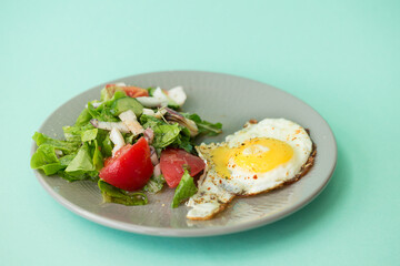 Fried egg with salad on a gray plate on a green background.