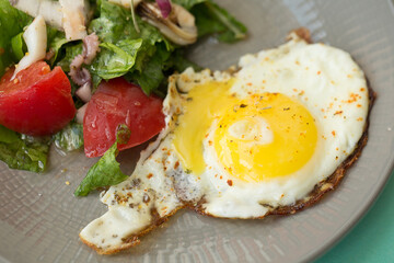 Fried egg with salad on a gray plate on a green background.