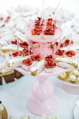 Front view of tower of delicious mousse desserts decorated with fresh strawberry, eclairs. French patisserie recipes. Beautiful yummy candy bar on wedding celebration. Concept of healthy bakery, diet.