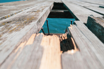 Rusty nails sticking out near a hole in an old wooden bridge over the blue water of a river (lake) close-up