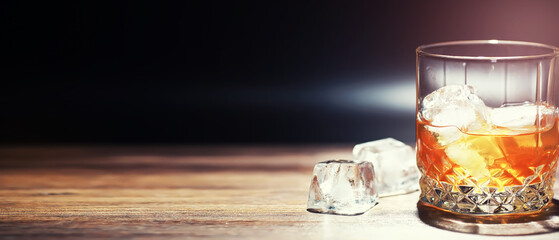 A glass of strong alcoholic drink with ice on a wooden bar counter. Whiskey with ice cubes. Glass with a chilled drink.