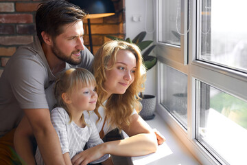 happy young family looking through the window at home, look at the street, happy together.
