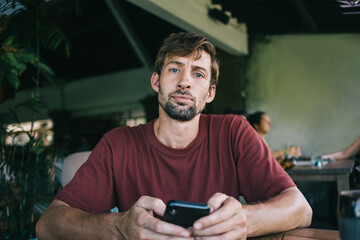 Serious young male with smartphone at table in cafe