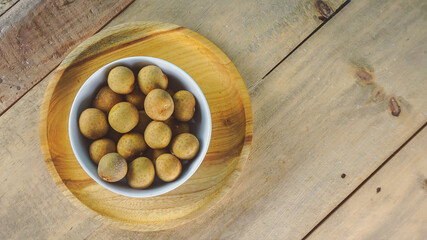 Overhead view of longan fruits on white bowl- wooden background