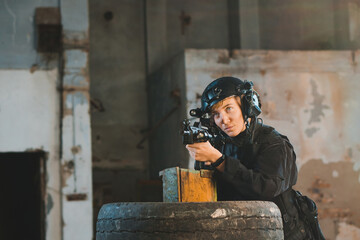 Young woman soldier in black uniform aiming with a rifle. Copy space.