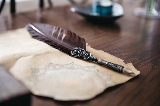 Close up of stylish handmade writing feather and old fashioned paper with monochrome mandala pattern on wooden table. Modern accessories for businessman for notes. Concept of unique birthday gift.