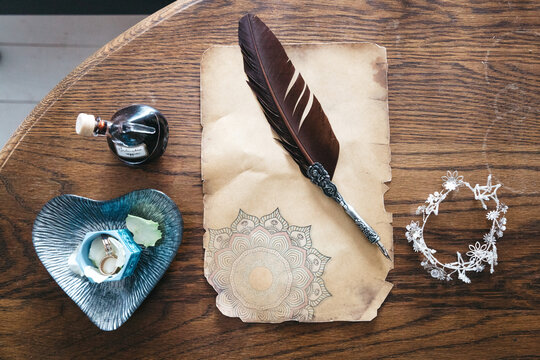 Top view of old paper, writing feather, precious anklet, wedding bands and perfume on wooden table. preparing for wedding day, bridal rituals before ceremony. Concept of unusual accessories and detail