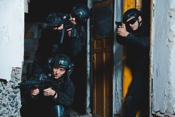 Three special forces soldiers in black uniform aiming with rifle and pistol from the corner