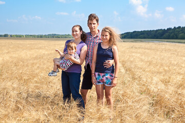 Young family with two daughters of different ages, preteen and infant girls, four people standing on yellow wheat field, full length portrait