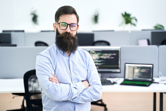 Confident computer programmer developer standing in IT office crossing hands on chest, working on a project in software development company or startup. High quality image.