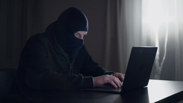 Hacker cracker in the hood in a dark room using computer virus program for cyber attack. Security concept.