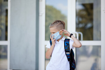 Schoolboy on the doorstep of school puts on a protective face mask. Back to school after quarantine
