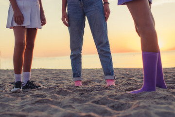 three young female friends standing on the beach  and looking at the sea on sunrise. close-up legs