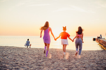 Three young girl  running along the sandy beach into the sea. Back view. Rest on the sea, sunbathing, healthy lifestyle.