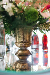Front view of golden antique vase with floral composition on table. Beautiful decoration of interior at restaurant. pretty details of decor on wedding celebration. Concept of fresh flowers and beauty.
