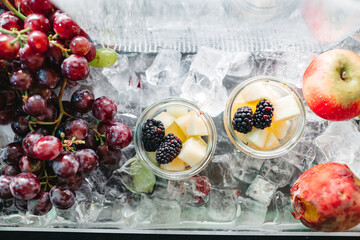 Top view of delicious fresh fruit in glassware, ice in freezer. Tasty juicy grapes, apple,...