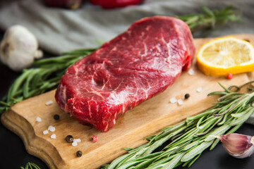Raw beef steak on a cutting board with spices. Creative atmospheric decoration.