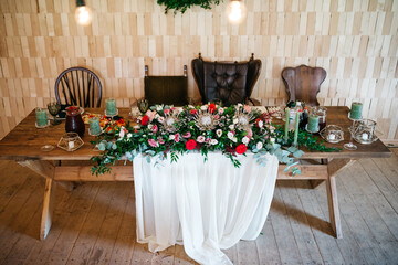 Front view of decorated wedding table for bride and groom with beautiful large floral composition. Celebration preparing in cozy restaurant. Details of table serving. Concept of authentic bridal style