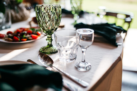 Close up of table serving, green goblet, and transparent water glass. Preparation for formal dinner, fancy restaurant. Decoration for elegant anniversary party. Concept of design, waiting for people.