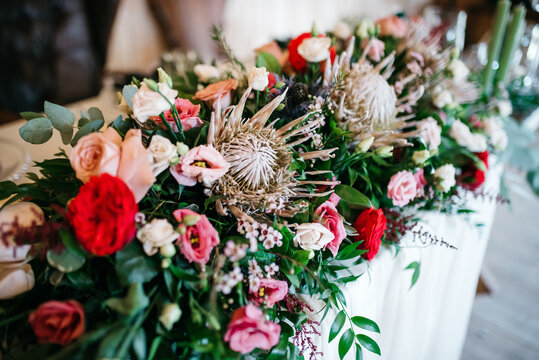 Close up of beautiful floral composition made of protea, pale pink eustoma, red roses and greenery. Charming interior decoration for wedding celebration. Concept of inspiration detail and atmosphere.