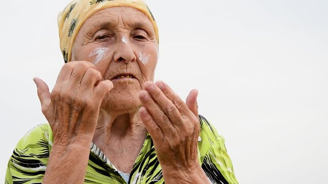 Cream on the old wrinkled face of the grandmother close up. An old grandmother uses an anti-wrinkle face cream. Old grandmother's cosmetic procedures. The inevitable aging process