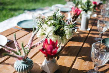 Close up of floral tiny bouquets, wooden table, goblets and dim blue plates. Beautiful wedding serving. Details of birthday dinner decoration. Family eating on backyard. Concept of everyday beauty.