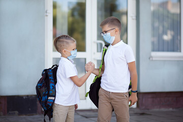 Fototapeta premium Primary school students greet on the doorstep of the school, observing social distance. Back to school after quarantine. New normal concept.