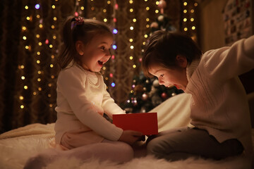 Family on Christmas eve at fireplace. Kids opening Xmas presents. Children under Christmas tree with gift boxes. Decorated living room with traditional fire place. Cozy warm winter evening at home.