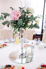 Front view of vase with floral composition made of eucalyptus and pale pink flower. Wedding table serving. Beautiful florist job. Restaurant adornment for birthday celebration. Concept of atmosphere.