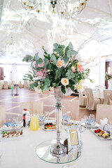 Front view of beautiful bouquet on decorated round table at restaurant on pompous celebration. Floral centerpiece on wedding party. Peopleless hall, gala night preparing. Concept of interior element.