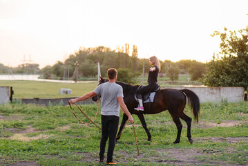 A young and pretty girl is learning to ride a thoroughbred Mare on a summer day at the ranch. Horse...